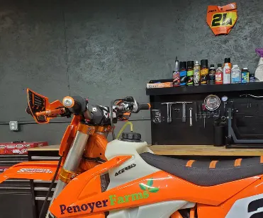 Orange dirt bike on a stand in the Cedar Motorsport Repair shop